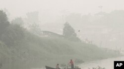 A man rows a boat on Siak River as thick haze from wildfires blanket the city in Pekanbaru, Riau province, Indonesia, Oct. 5, 2015. 