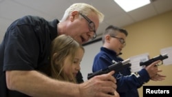 Instructor Jerry Kau shows student Joanna Zuber how to load a magazine into a handgun alongside Sam Minnifield during a Youth Handgun Safety Class at GAT Guns in East Dundee, Illinois, April 21, 2015.