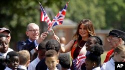FILE - U.S. first lady Melania Trump and Philip May, the husband of British Prime Minister Theresa May, wave their respective national flags during a visit to British military veterans at The Royal Hospital Chelsea in central London, July 13, 2018.