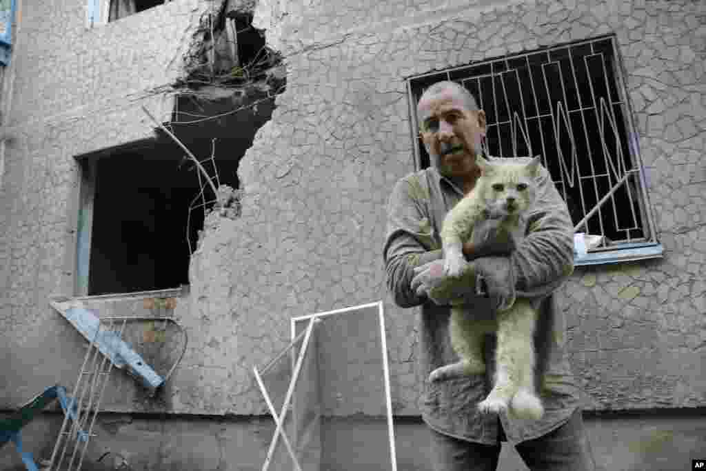 Valery, who gave only his first name, carries his injured cat in front of his damaged house after shelling, in the city of Slovyansk, June 30, 2014.