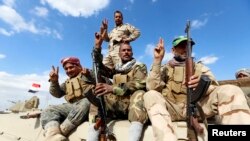 Members of the Iraqi security forces and Shi'ite fighters sitting on a military vehicle gesture in the town of Hamrin, in the Salahuddin province, March 3, 2015.