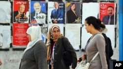 Women walk past a wall plastered with electoral campaign posters two days before the first round of the presidential elections in Tunis, Tunisia, Nov. 21, 2014.