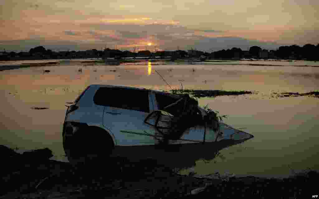 The sun sets behind the wreckage of a vehicle submerged in floodwaters in Joso city, Ibaraki prefecture, Japan. Thousands of rescuers arrived in the deluged city north of Tokyo to help evacuate hundreds of trapped residents and search for 12 people missing after torrential rains triggered massive flooding.
