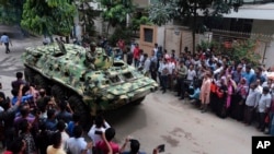 An armored vehicle drives past members of the press after an operation against militants who took hostages at a restaurant popular with foreigners in Dhaka, Bangladesh, Saturday, July 2, 2016.