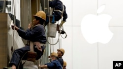 Workers clean windows near Apple's retail store in Beijing. China reported an unexpected contraction in exports in March, raising the danger of job losses as Beijing tries to overhaul its slowing economy, April 10, 2014.