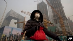 A woman wears a mask as she walks past a construction site as smog continues to choke Beijing, China, Jan. 6, 2017. 