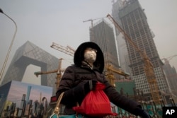 FILE - A woman wears a mask as she walks past a construction site as smog continues to choke Beijing, China, Jan. 6, 2017.