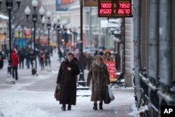 FILE - Women pass a currency exchange kiosk on a street in Moscow, Russia, Jan. 18, 2016.