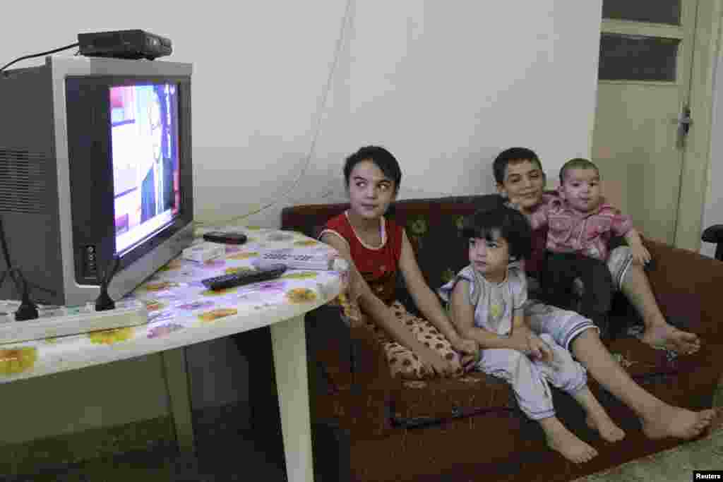 Young Syrian refugees watch a news broadcast on the Syria crisis with their father (unseen) at their temporary home at the Al Hussein refugees camp in Amman, Jordan, August 29, 2013.
