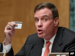 FILE - Sen. Mark Warner, D-Va., chairman of the Senate Banking Subcommittee on National Security and International Trade and Finance, displays his bank card at a hearing, Feb. 3, 2014, after the theft of consumers’ data at retailers such as Target Corp and Neiman Marcus during the holiday shopping season.
