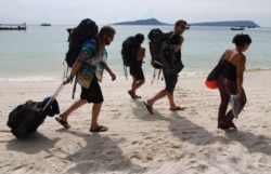 FILE - Tourists walk along a beach on Koh Rong island in Sihanoukville province on October 31, 2019. (Photo by TANG CHHIN Sothy / AFP)