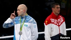 Silver medalist Vassiliy Levit of Kazakhstan reacts to the audience as gold medalist Evgeny Tishchenko of Russia stands at attention for the singing of the national anthem at the 2016 Olympics in Rio de Janeiro, Aug. 15, 2016.