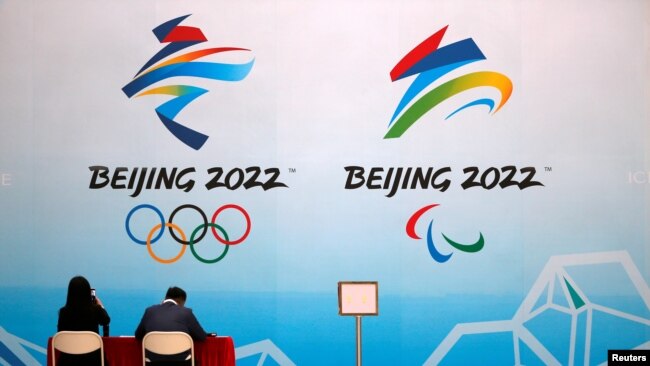 FILE - Staff members sit near a board with signs of the 2022 Olympic Winter Games, at the National Aquatics Center in Beijing, China, April 1, 2021.