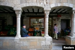FILE - An old man rests under the medieval arches in the old city of Besalu, near Girona, in the northeastern region of Catalonia, Spain, April 5, 2014.