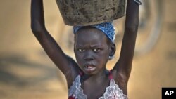 FILE - A young displaced girl carries a bucket of water back to her makeshift shelter at a United Nations compound which has become home to thousands of people displaced by the recent fighting, in the Jebel area on the outskirts of Juba, South Sudan, Dec. 31, 2013.