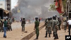 Guinea security forces, center, face people rioting and burning rubbish and other goods in the streets of Conakry, April 13, 2015.