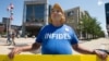 Bob Kunst of Miami Beach, Fla. wears a Hillary Rodham Clinton mask and holds an anti-Hillary poster outside the Quicken Loans Arena in Cleveland, Aug. 5, 2015.