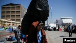 Un réfugié porte sa valise pour monter à bord d'un bus à destination d'un autre pays d'accueil au port de Piraeus, près d’Athènes, en Grèce, le 31 mars, 2016.