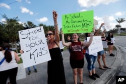 Angelina Lazo, 18, center, a senior at Marjory Stoneman Douglas High School, holds a sign with other students and parents at an intersection near the Marjory Stoneman Douglas High School in Parkland, Fla.