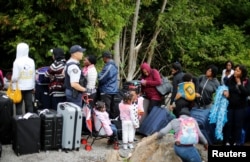 FILE - A Royal Canadian Mounted Police officer announces to a group of asylum seekers that identified themselves as from Haiti, that they will be crossing illegally into Canada as they wait in line to to enter at the U.S.-Canada border in Champlain, New York, Aug. 7, 2017.