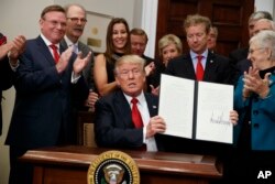 President Donald Trump shows an executive order on health care that he signed Oct. 12, 2017. The Trump administration says it’s freezing payments under an ‘Obamacare’ program that protects insurers with sicker patients from financial losses, a move expected to add to premium increases next year.