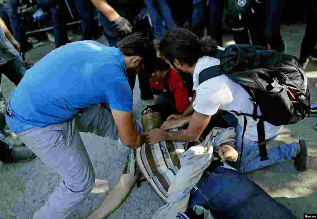 Migrants help an injured migrant during a stampede to board a bus in Tovarnik.