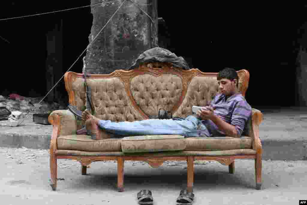 A rebel fighter looks at his smartphone lying on a sofa in Bustan Pasha neighborhood of Syria&#39;s northern city of Aleppo. 