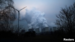 Uap air membubung dari menara-menara pendingin PLTU Jaenschwalde milik Lausitz Energie Bergbau AG, yang tak jauh dari turbin angin di Jaenschwalde, Jerman, 24 Januari 2019.