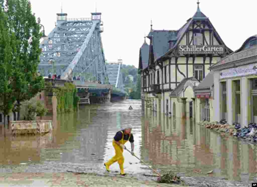 Một người giúp dọn dẹp bờ sông Elbe phía trước cây cầu lịch sử Blaues Wunder (trái) ở Dresden, ngày 6/6/2013. Cây cầu bị đóng không cho thông xe. (AP Photo/Jens Meyer)