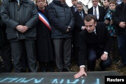 French President Emmanuel Macron places a pebble on a vandalized tomb to a pay a tribute during a visit at a desecrated Jewish cemetery in Quatzenheim, France, Feb. 19, 2019.