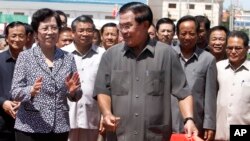 Cambodian Prime Minister Hun Sen, center, cuts the ribbon with Chinese Ambassador to Cambodia Bu Jianguo, left, during the inauguration ceremony of a friendship bridge between Cambodia and China in Takhmao, Kandal provincial town, south of Phnom Penh, Cambodia, Monday, Aug. 3, 2015. The bridge across the Tonle Bassac River opened to the public on Monday. (AP Photo/Heng Sinith)