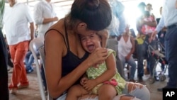 FILE - A Venezuelan woman holds a girl at a health post for migrants in Cucuta, along Colombia's border with Venezuela, July 16, 2018.
