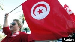 FILE - A woman waves a Tunisia flag during a rally to protest against religious and political violence in Tunis, Oct. 22, 2012. 