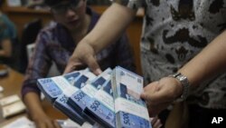 An employee shows stacks of rupiah banknotes at a money changer in Jakarta, Indonesia, Aug. 23, 2013. 