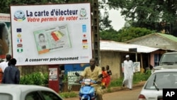 People walk in front of posters for the presidential elections and instructions on the voting card, Conakry, 25 Jun 2010