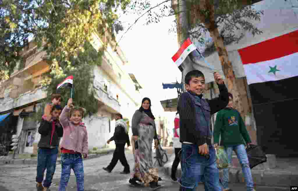 Syrian children wave national flags as they walk in al-Hellok neighbourhood in the northern city of Aleppo, after Syrian army forces replaced the Kurdish People's Protection Units (YPG) which had previously been in control.