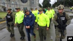This undated photo released by Colombia's National Police shows officers escorting a man whom police identified as Ecuadorean drug trafficker Edison Prado after his April 2017 arrest on an indictment by a Florida federal court. A few months after his arrest in a DEA-organized raid, Prado showed up on a list, with more than 20 other suspected traffickers, of rebels of the Revolutionary Armed Forces of Colombia. FARC claimed them as jailed members of its now-disbanded insurgency, even though they have no known history of rebellion.