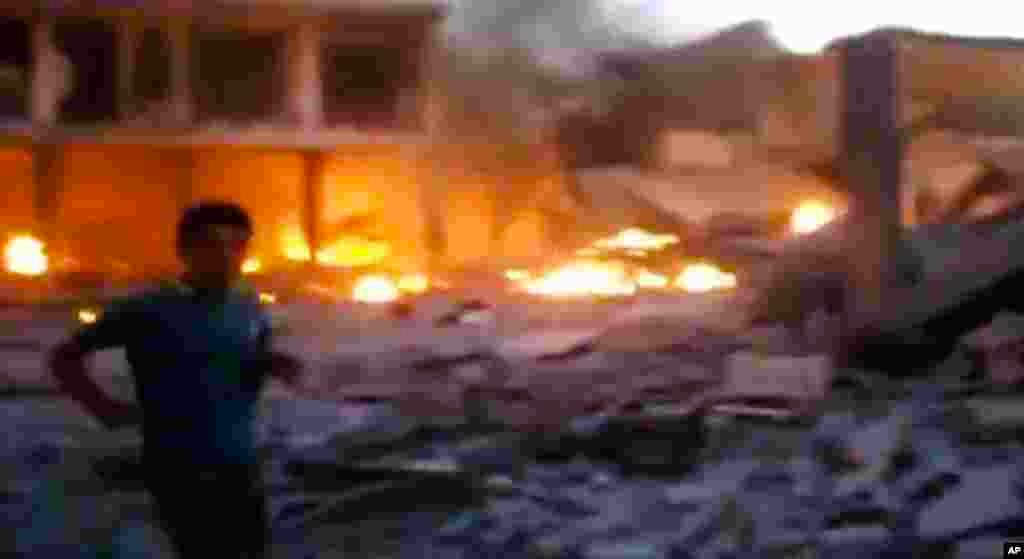 This image taken from video obtained from the Shaam News Network shows a Syrian man walking near destruction and fire caused by a bomb that hit Binnish town, Idlib province, Sept. 5, 2013. 