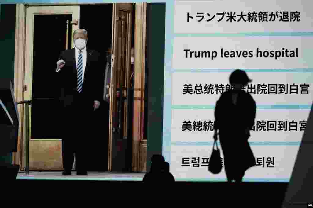 People walk past a screen in Tokyo, Japan, showing the news report that President Donald Trump has left a hospital to return to the White House after receiving treatments for COVID-19.