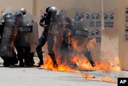 巴黎防暴警察试图扑灭抗议者投掷燃烧弹点起的火焰。（2018年5月1日）