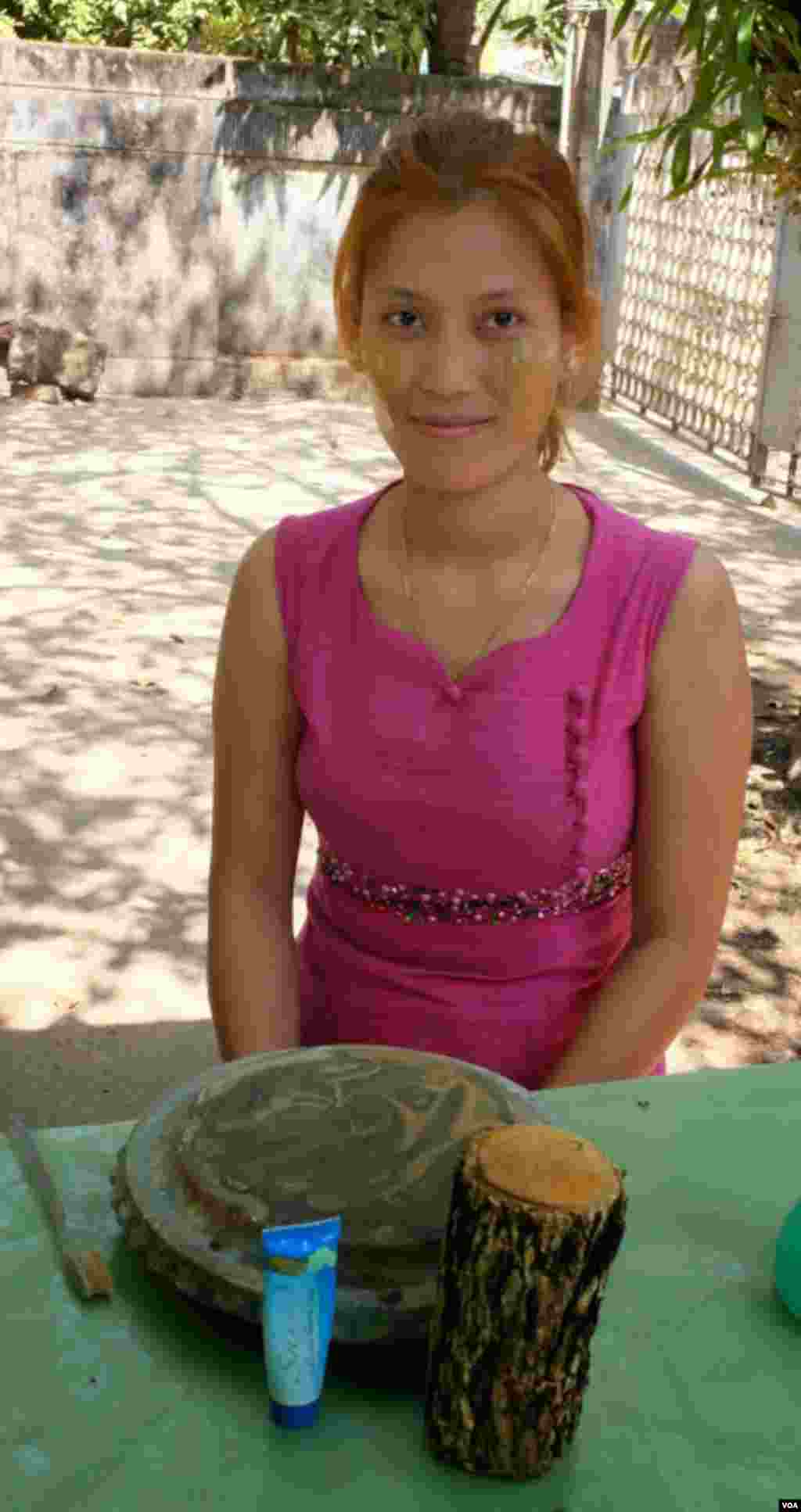 A woman poses with freshly made thanaka next to a tube of pre-made thanaka cream. (Steve Herman/VOA News)