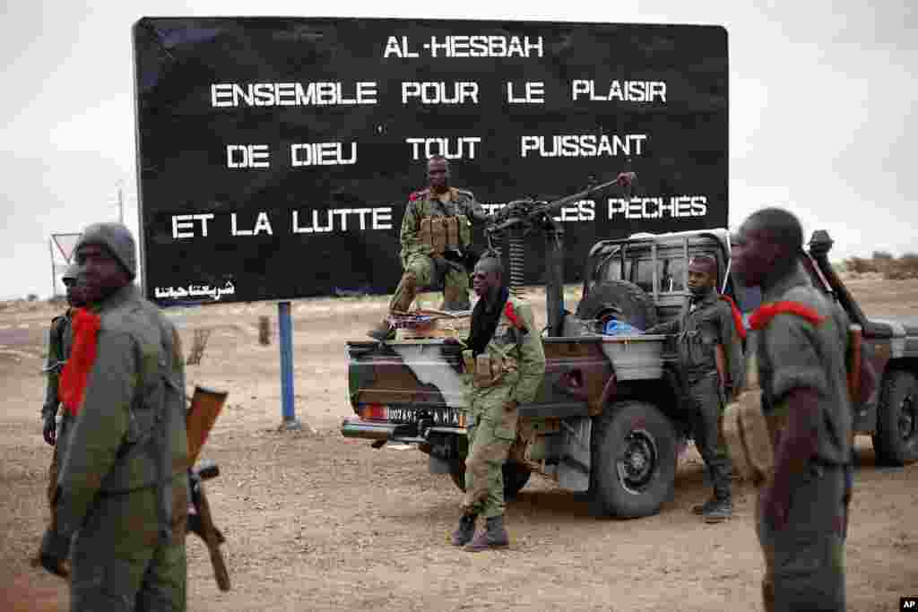 马里士兵守卫在加奥市进口，标语牌上写有警告伊斯兰极端分子的话：共享全能上帝的福分，向罪恶作斗争