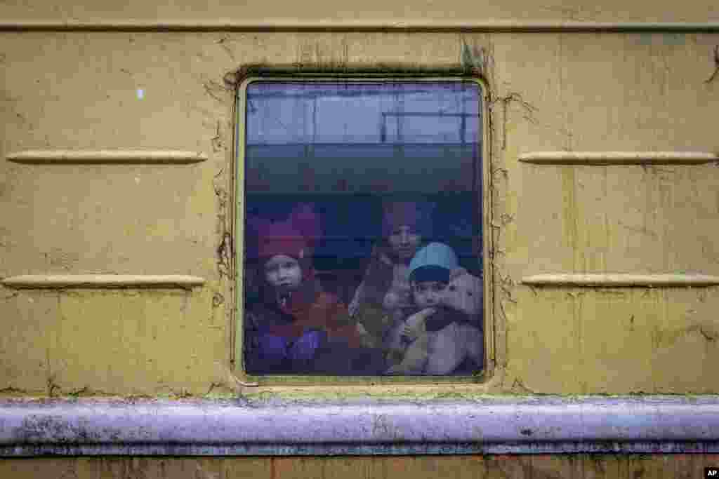 Children Vlada, left, Katrin and Danilo look out of a window of an unheated train for an emergency evacuation which is traveling from Kharkov to Lviv as it stops at the Kyiv railway station in Kyiv, March 3, 2022.