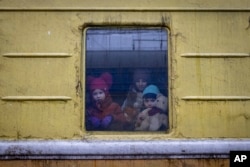 Anak-anak Vlada (kiri), Katrin dan Danilo melongok dari jendela gerbong kereta api tanpa penghangat, saat evakuasi darurat dari Kharkov ke Lviv dan berhenti di stasiun kereta api Kyiv di Kyiv, Ukraina, Kamis, 3 Maret 2022 (Foto AP/Andriy Dubchak)
