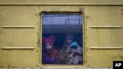 Los niños Vlada, a la izquierda, Katrin y Danilo miran desde la ventana de un vagón de sin calefacción de un tren de evacuación de emergencia que viaja de Járkov a Leópolis, cuando se detuvo en la estación de tren en Kiev, Ucrania, el 3 de marzo de 2022.