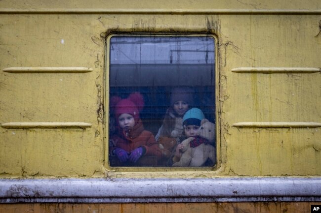 Anak-anak Vlada (kiri), Katrin dan Danilo melongok dari jendela gerbong kereta api tanpa penghangat, saat evakuasi darurat dari Kharkov ke Lviv dan berhenti di stasiun kereta api Kyiv di Kyiv, Ukraina, Kamis, 3 Maret 2022 (Foto AP/Andriy Dubchak)