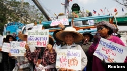 Farmers hold signs in front of a combine harvester during a rally demanding the Yingluck administration resolve delays in payment from the rice-pledging scheme outside the Commerce Ministry in Nonthaburi province, on the outskirts of Bangkok, Feb. 6, 2014