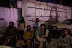 FILE - Taliban fighters sit in front of a mural depicting a woman behind barbed wire, in Kabul, Afghanistan, Sept. 21, 2021.