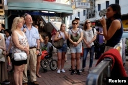 FILE - Tour guide Alla Lau, right, speaks to tourists who join a free tour at Mong Kok district in Hong Kong, China, Aug. 6, 2017.