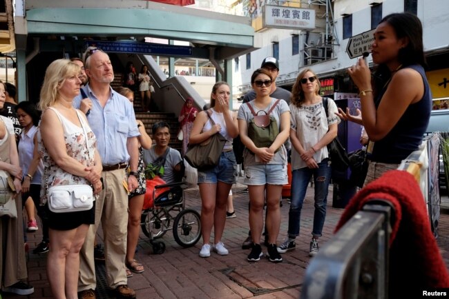 FILE - Tour guide Alla Lau, right, speaks to tourists who join a free tour at Mong Kok district in Hong Kong, China, Aug. 6, 2017.